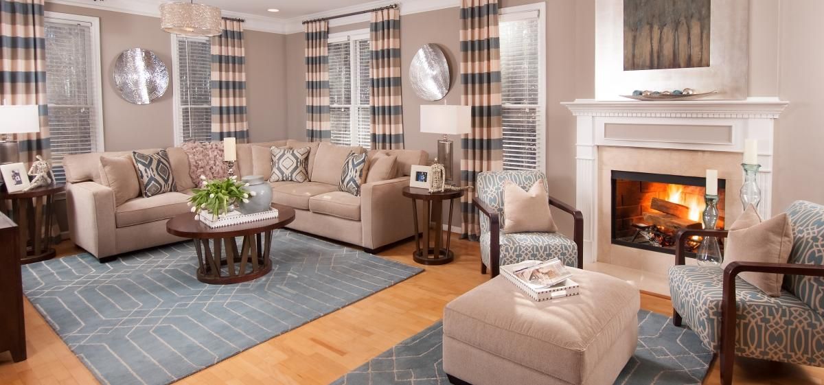 Living room area with brown furniture, striped curtains, metallic accents and blue rugs on top of light wooden floors