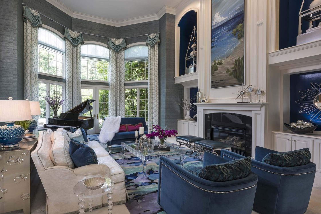 Large living room with blue accents and furnishings and tall windows and draperies