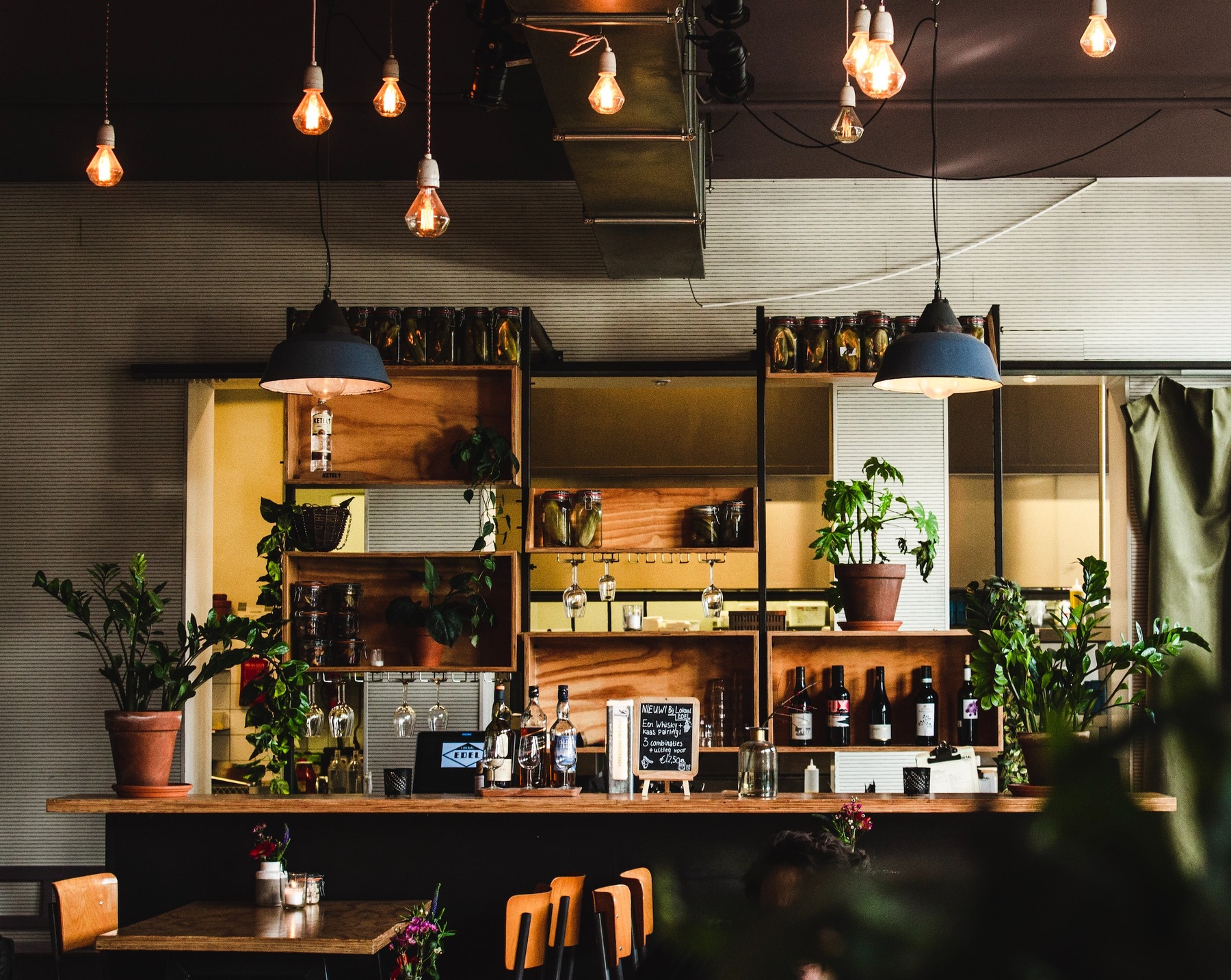 A bar with plants and hanging lights, tables and chairs