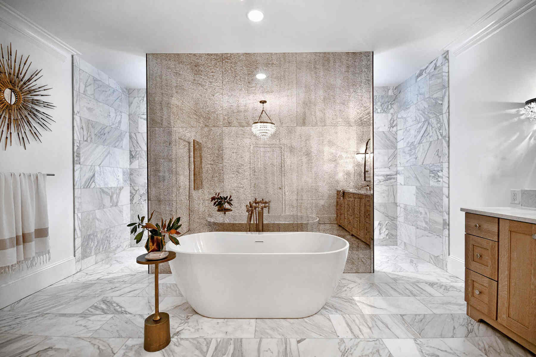 Bathtub placed on the center of a bathroom with multiple textured walls and marble flooring
