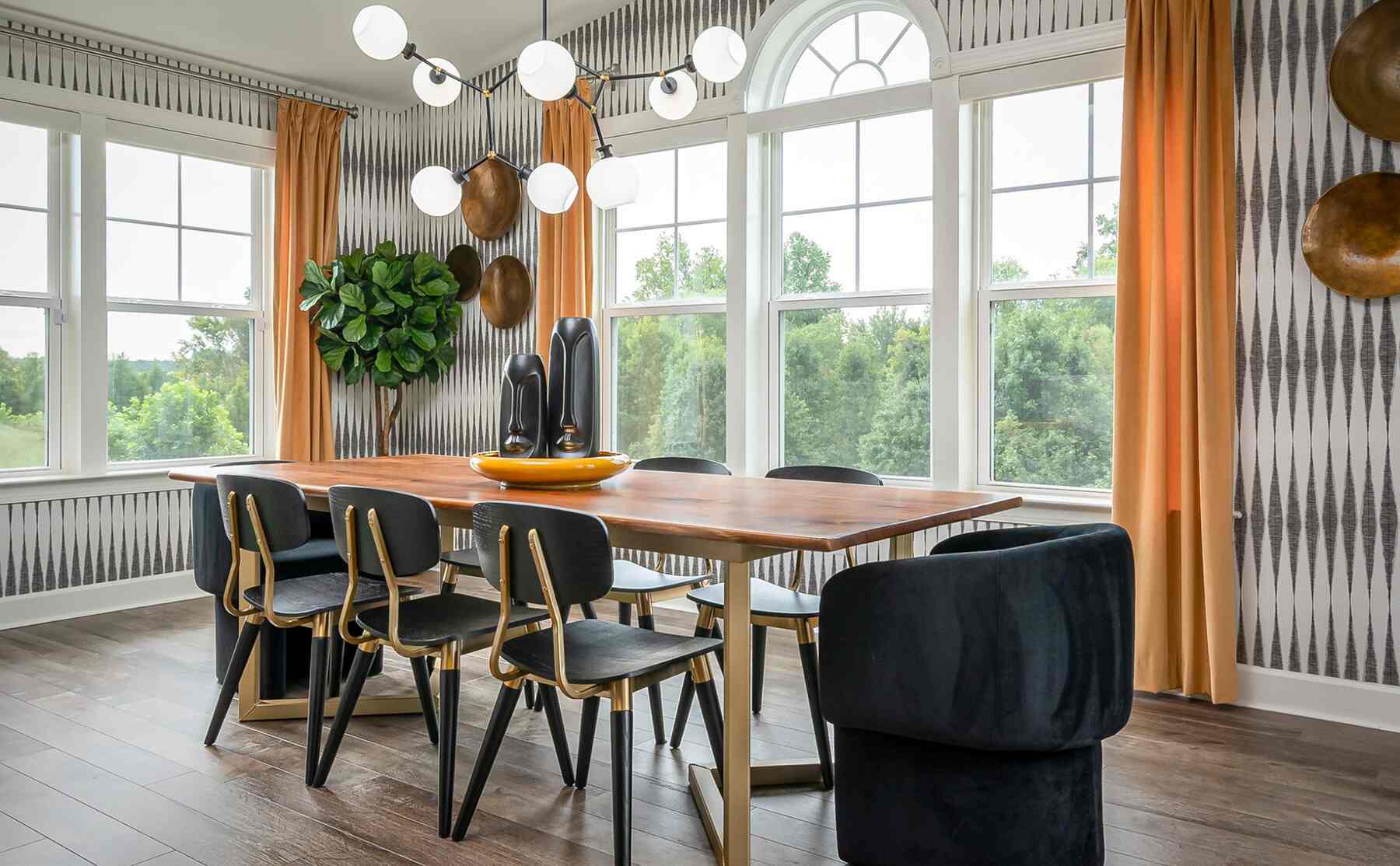 Wooden dining table with sleek black and gold chairs and drop bulb chandelier