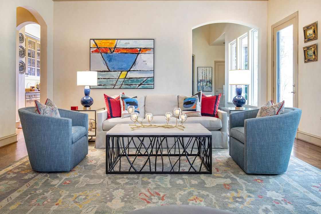A living room with a statement piece of art hanging on the wall, blue and grey sofas, and center table